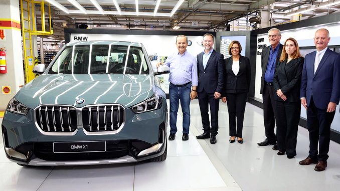 Executivos em pé ao lado do BMW X1 dentro da fábrica.